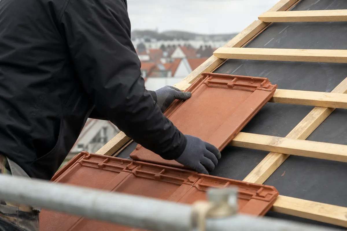 Mains d&rsquo;un couvreur posant des tuiles mécaniques neuves sur un liteaunage rénové