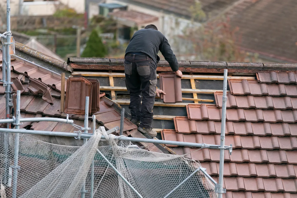Artisan de dos remplaçant des tuiles sur un toit pavillonnaire, échafaudage au premier plan